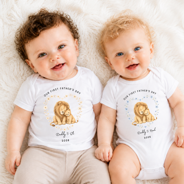 Two babies wearing 'Our First Father's Day' t-shirts with lion graphics on a fluffy white surface.