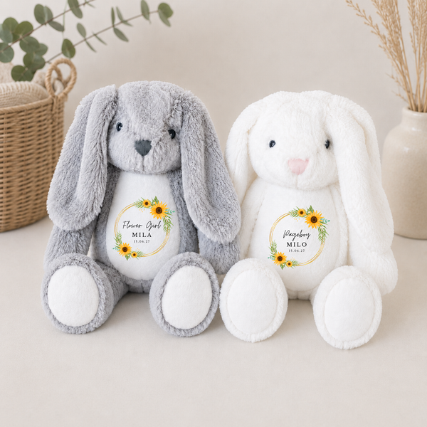 Two plush bunny toys, one gray and one white, with personalized sunflower wreath pattern on a neutral background.