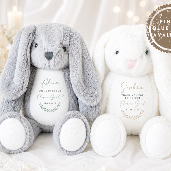 Two plush bunny stuffed toys posed together on a soft white fabric surface. The left bunny is light gray with a white belly and grey nose; the right bunny is white with a pink nose.